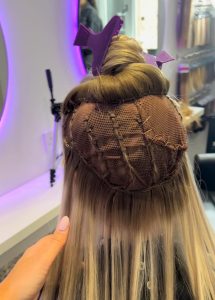 back of a girls head sat in a salon chair with a mesh and clip on her brown and light blonde hair undergoing hair treatment